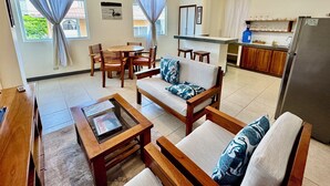 A living room with a sofa, coffee table, and dining area with chairs. There is a kitchen area with a refrigerator, sink, and counter. - This two-bedroom is a perfect island getaway. (Puerto Ayora, Santa Cruz Island)