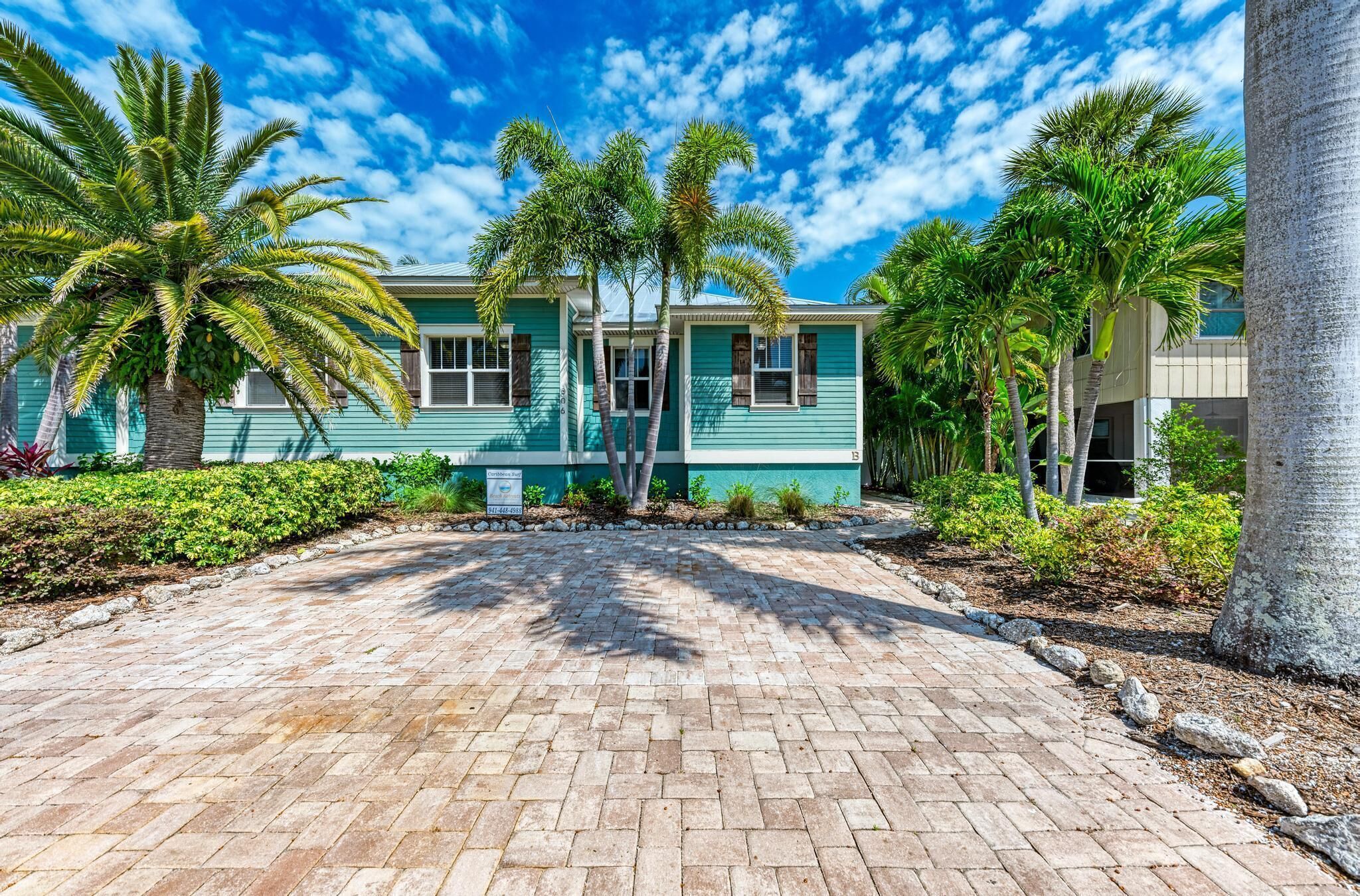 A beachfront property with a paved driveway, palm trees, and a turquoise building.