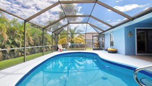 A swimming pool with a glass enclosure, surrounded by palm trees and a clear sky. - Beautiful 3 bed 2 bath, Heated Pool, Minutes from the Ocean (Sebastian)