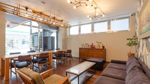 A spacious living area with a dining table, chairs, a sofa, and a bench. There is a large window providing natural light and a view of the outside. - The OneFive Tokyo Shibuya (Tokyo)