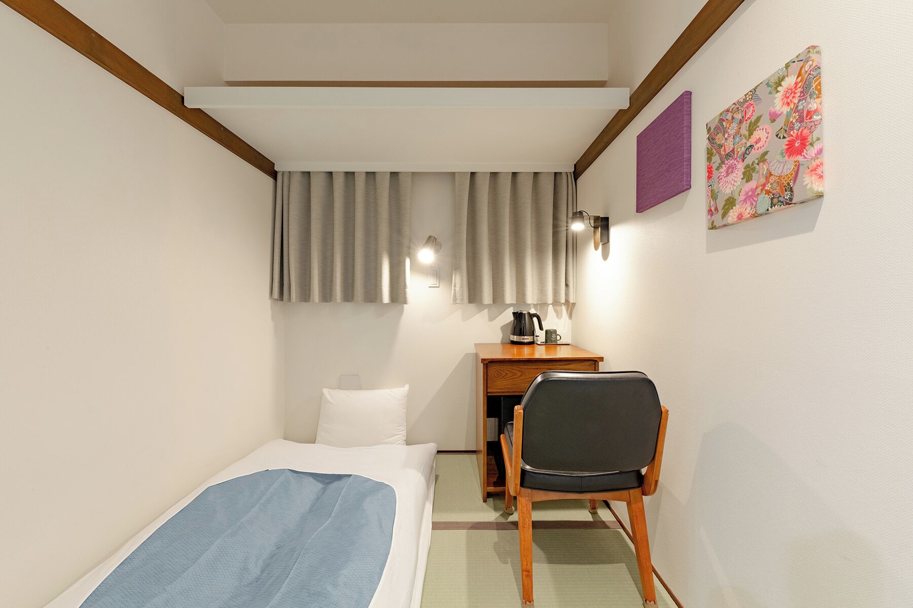 A hotel room with a bed, a desk with a chair, a nightstand, a lamp, and a painting on the wall.