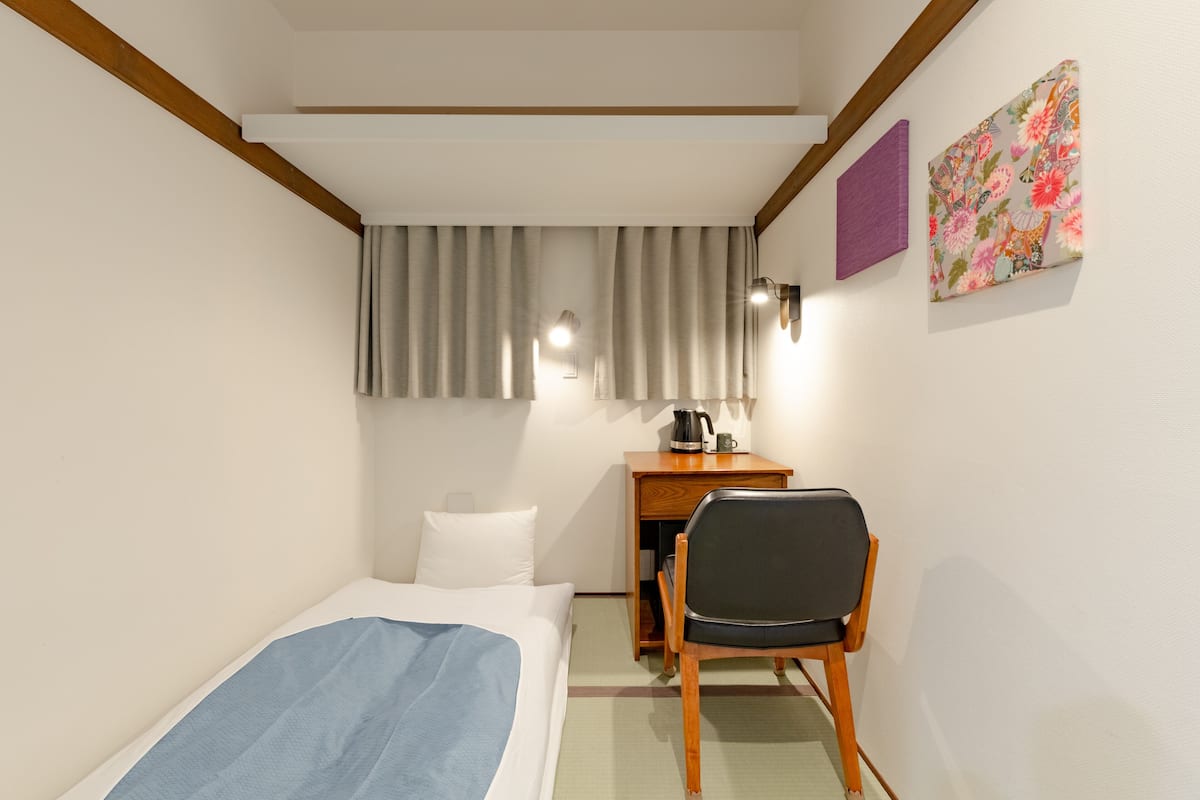 A hotel room with a bed, a desk with a chair, a coffee maker, and a curtain.