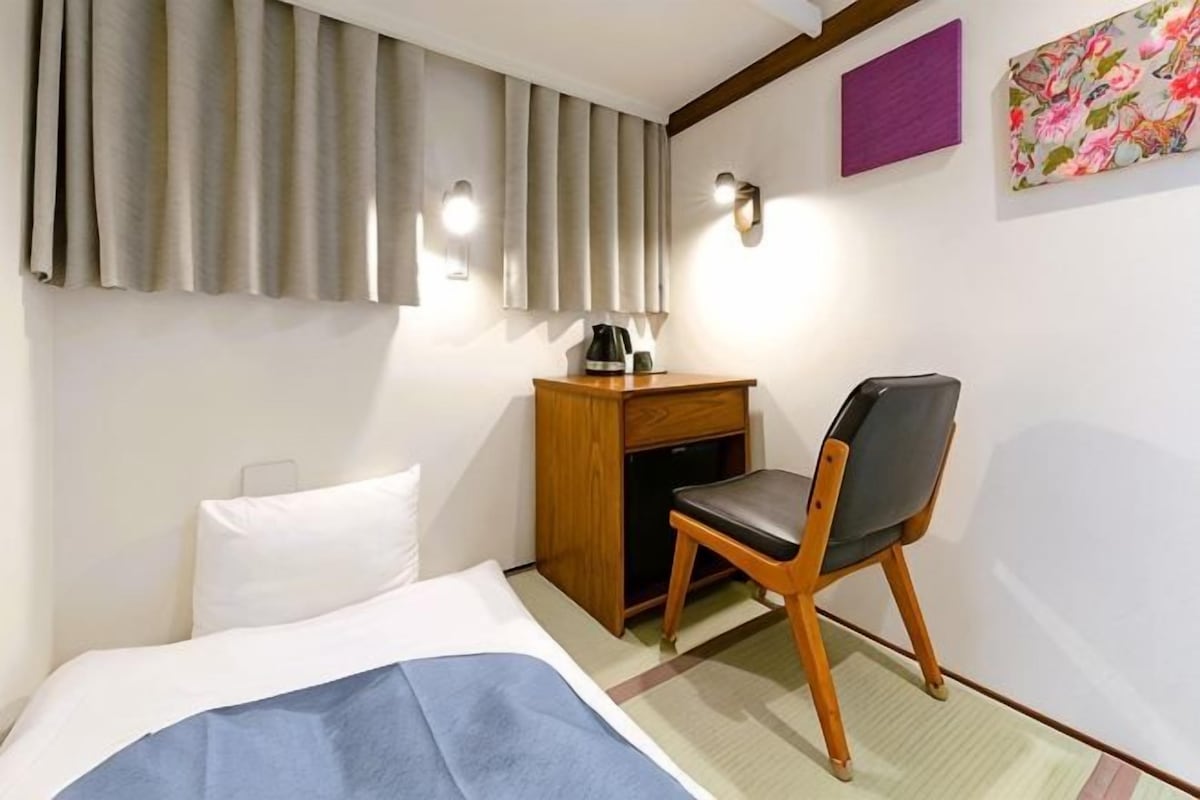 A hotel room with a bed, a desk with a chair, a coffee maker, and a painting on the wall.