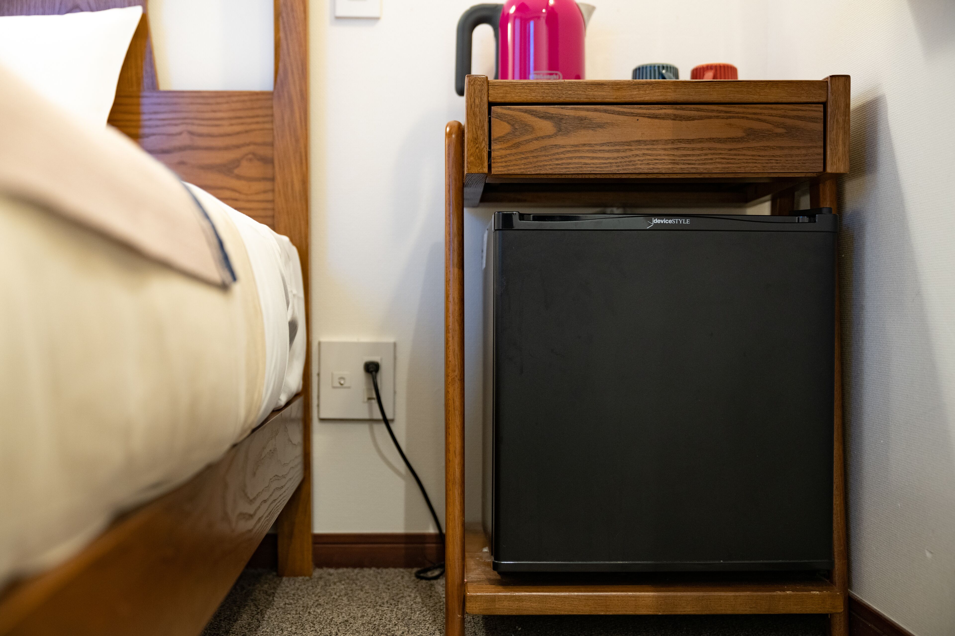 Una habitación pequeña con cama, una mesita de noche de madera y un refrigerador negro.