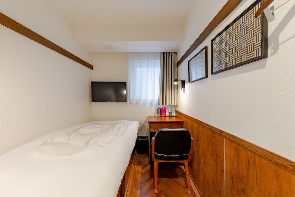 A hotel room with a bed, a desk with a chair, a television, and a patterned wall decoration.