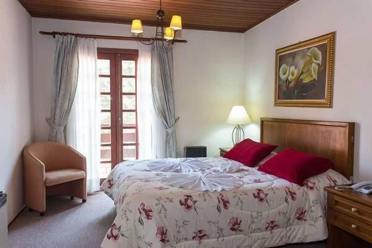 Quarto com cama, cadeira, mesa de cabeceira, luminária e um quadro na parede.
