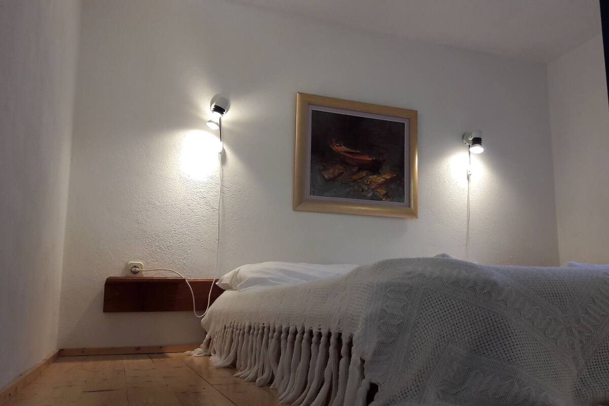 Une chambre à coucher avec un lit, un tableau accroché au mur et deux lampes fixées au mur.