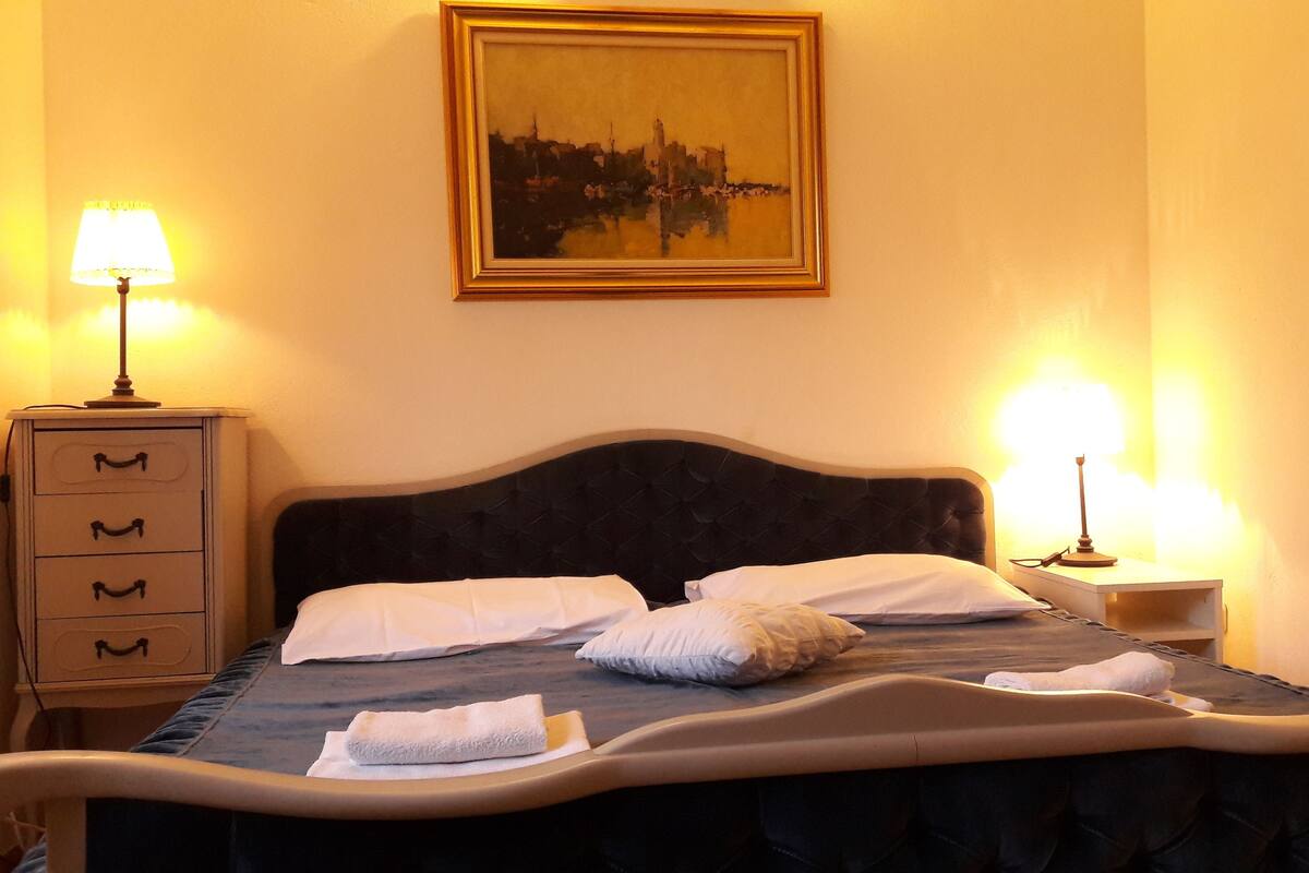 Une chambre d’hôtel avec un lit, deux lampes de chevet, une table de chevet, une commode et un tableau au mur.