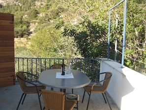 An outdoor dining area with a round table and four wicker chairs, surrounded by a blue metal railing.