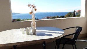 A round table with four white mugs and a clear vase with dried flowers, positioned on a balcony overlooking a coastal view with houses and mountains in the distance. - Apartmani Bako Komiza (Komiza)
