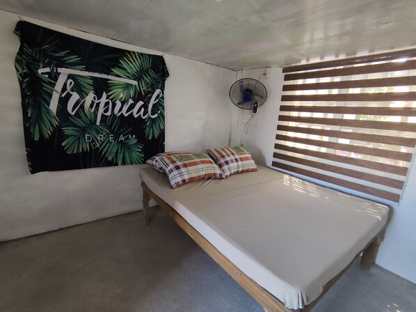 Una habitación con una cama, un ventilador de pared y una ventana con persianas.