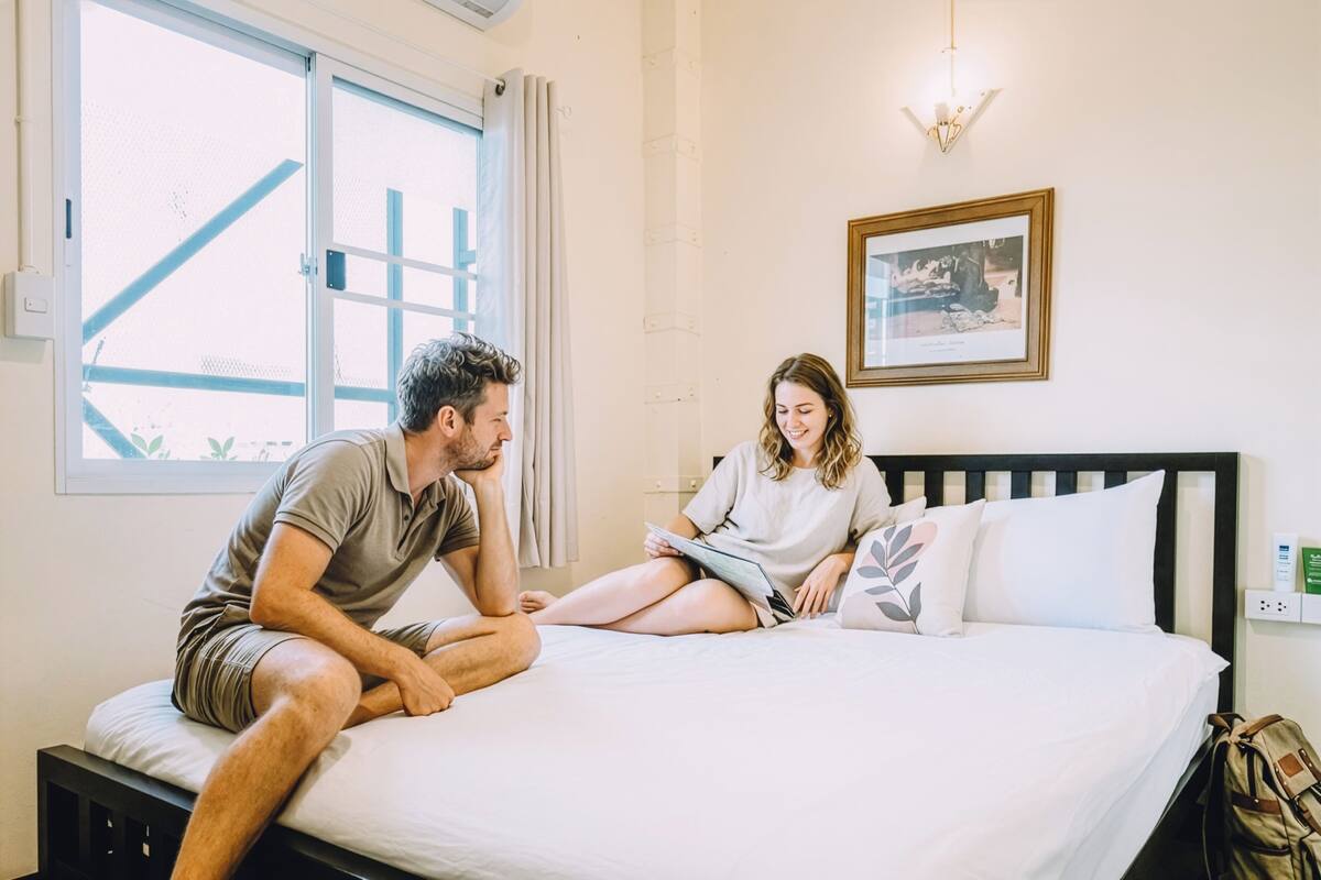 Een kamer met een bed, een raam, een lijst met een afbeelding aan de muur en een stopcontact.