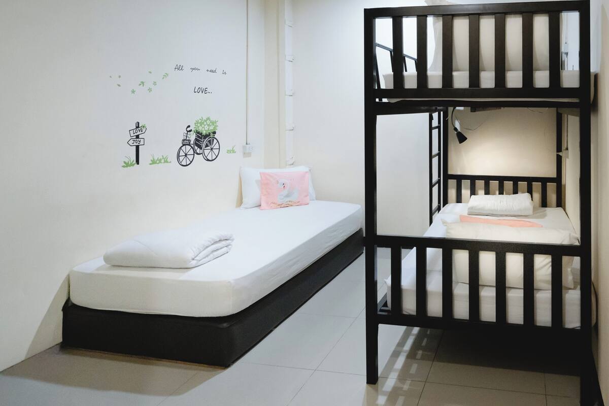 Een slaapkamer met een stapelbed, een enkel bed, een muursticker en een kleine plant.