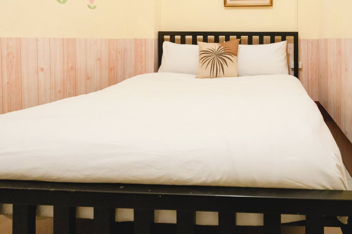 Een bed met witte beddengoed, een houten hoofdbord en een decoratief kussen.