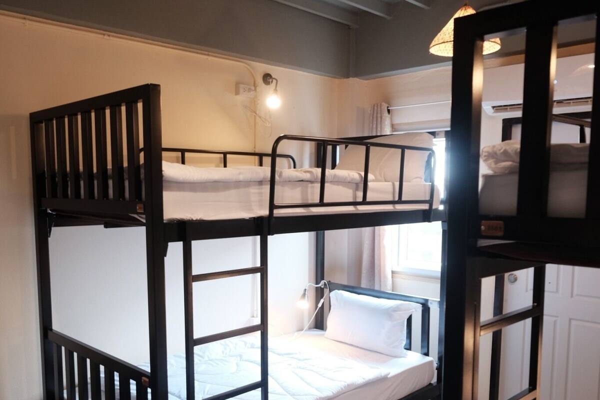 Een slaapkamer met stapelbed, een plafondlamp en een raam.