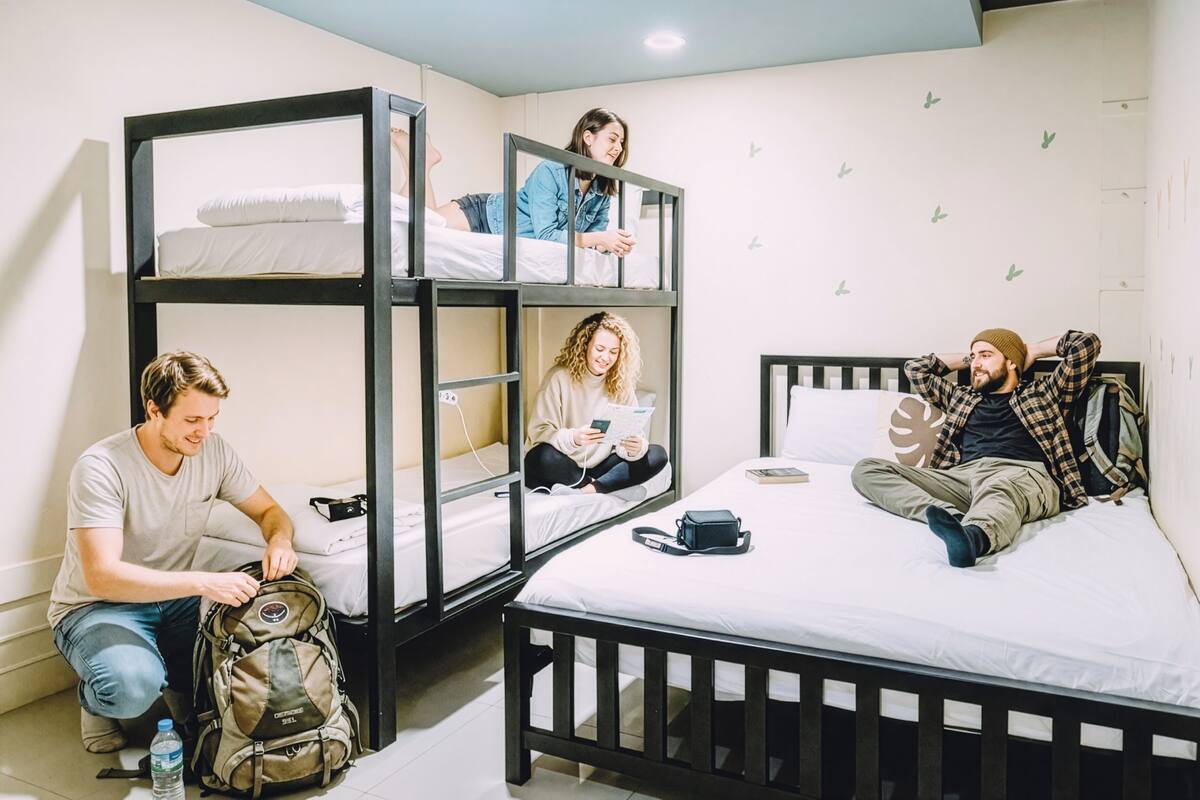 Een studentenkamer met stapelbedden, een eenpersoonsbed en een klein tafeltje.