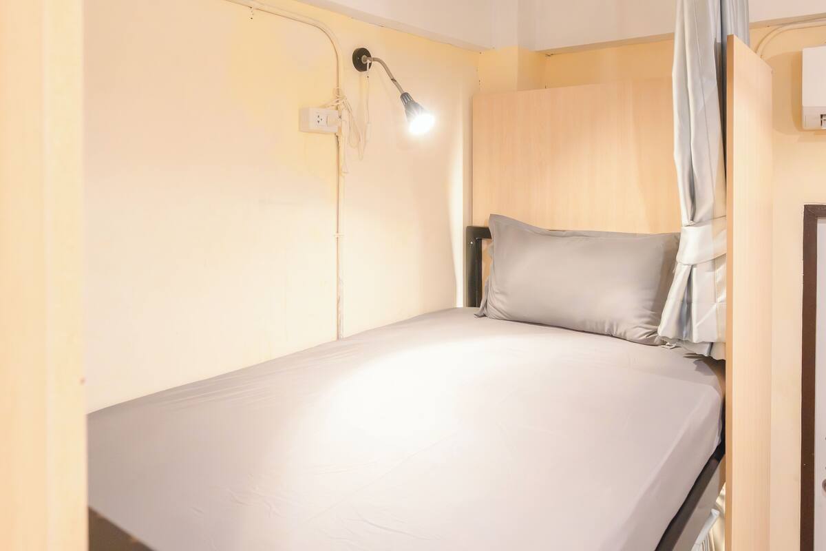 Een enkel bed met hoofdeinde, een bedlampje en een gordijn.
