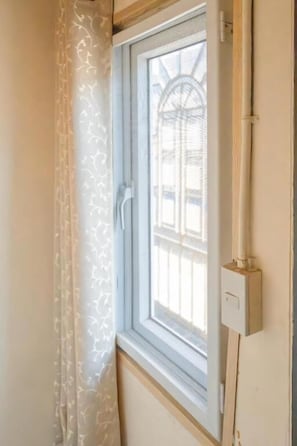 A window with a metal frame, a curtain, and a wall-mounted electrical outlet.