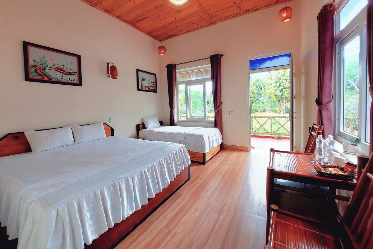 A room with two beds, a wooden ceiling, and a balcony with a table and chairs.