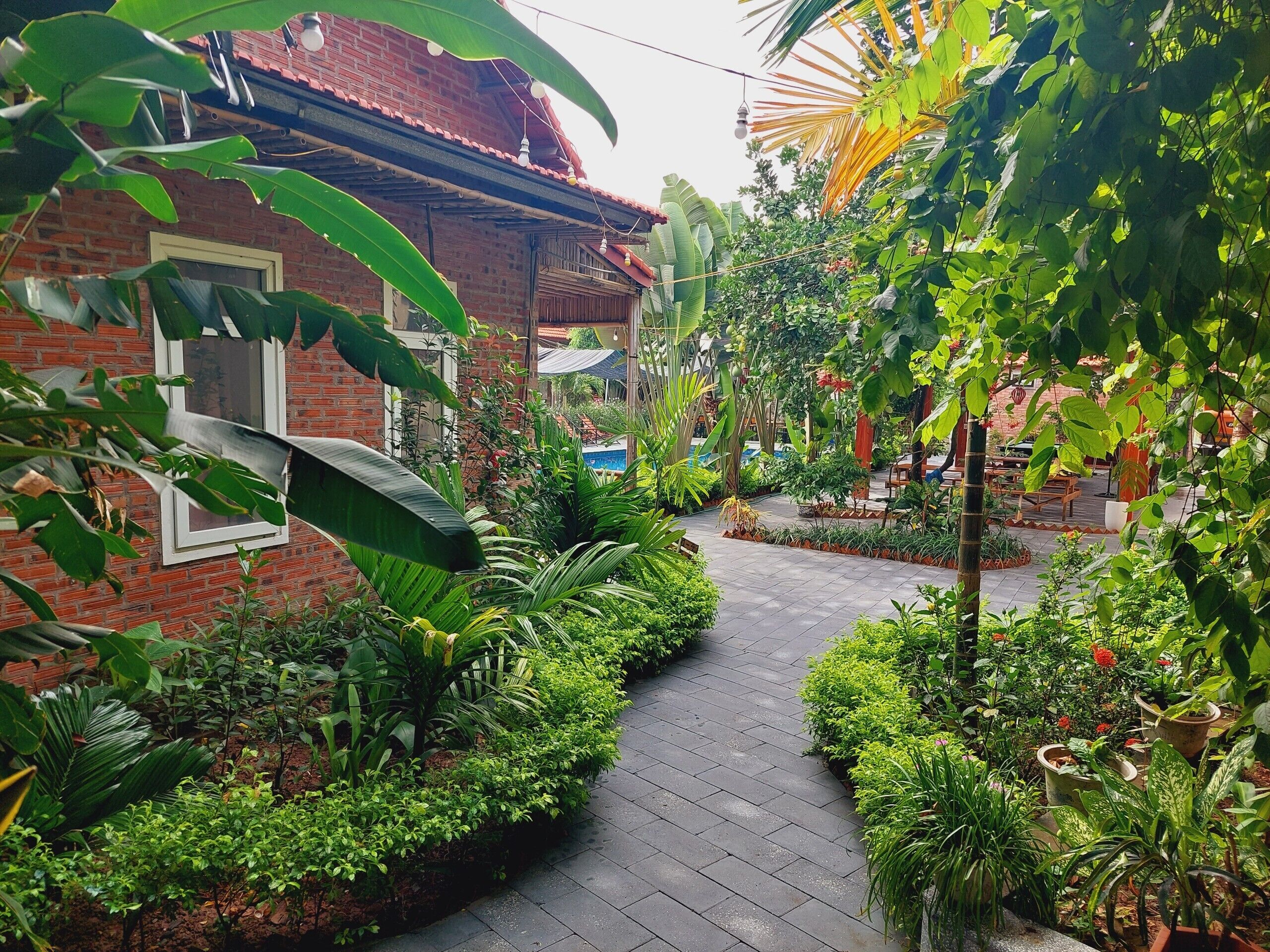 A brick building with a tiled roof, surrounded by lush greenery and a paved pathway.