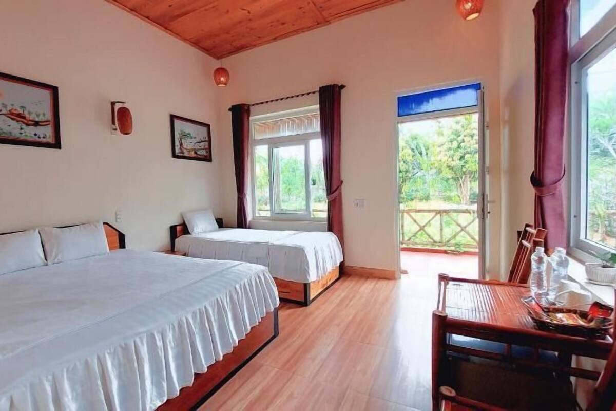 A room with two beds, a wooden ceiling, a window with curtains, and a table with chairs.