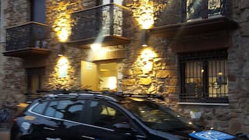 A black car parked in front of a stone building with illuminated windows and balconies.