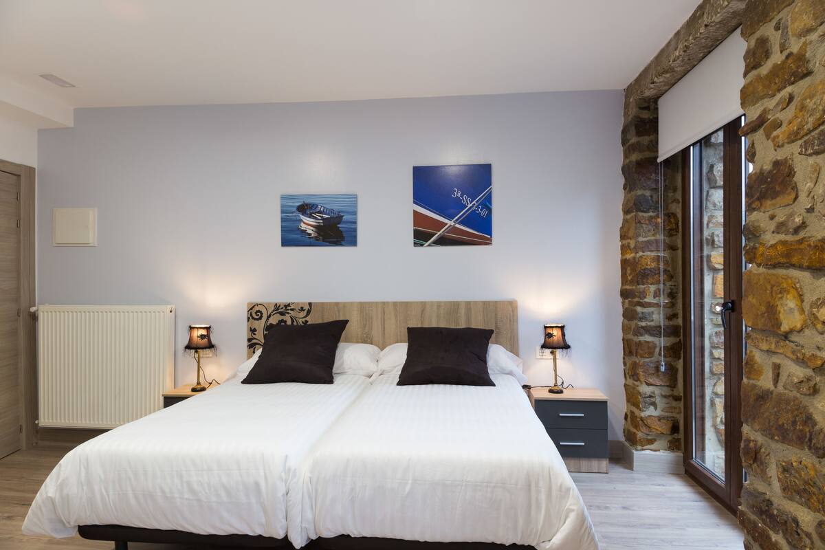 A double bed with white bedding, two bedside tables with lamps, a wooden headboard, and two wall-mounted artworks depicting boats.