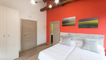 A bedroom with a bed, two doors, and a red wall with two landscape paintings.