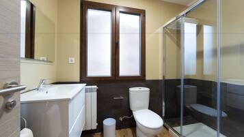 Een badkamer met een witte wastafel, een toilet, een douchecabine met glazen wanden en een raam met geëtste glasschijf.
