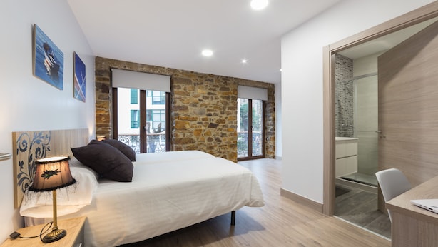 Un dormitorio con cama, escritorio, lámpara y pared de piedra.