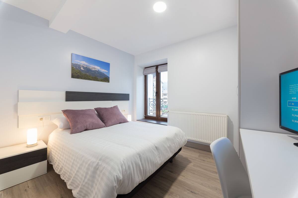 A bedroom with a bed, bedside table, and a desk with a chair.