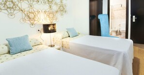 Habitación de hotel con dos camas, una lámpara de pared y un baño visible a través de una puerta abierta.
