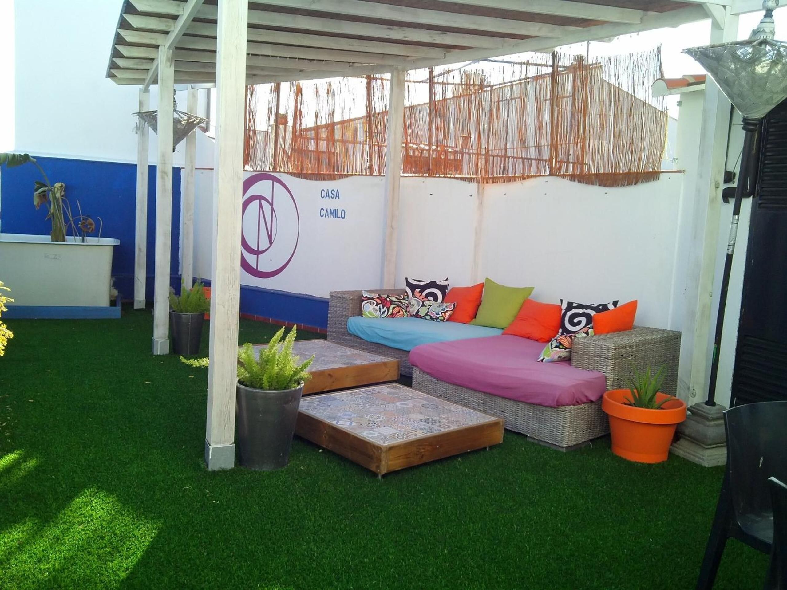 A covered outdoor seating area with a sofa and cushions, a small table, and potted plants.