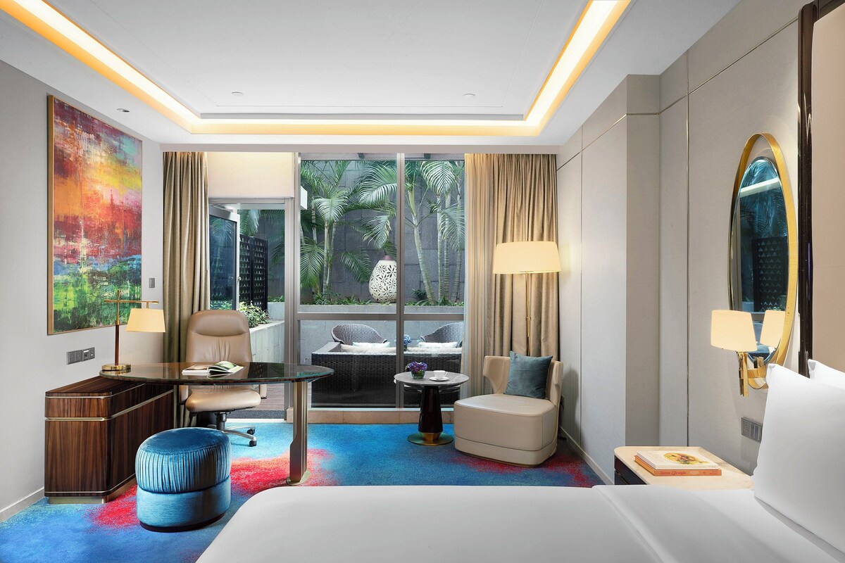 Habitación de hotel con ventana grande, escritorio, silla, sofá, mesita y cama.