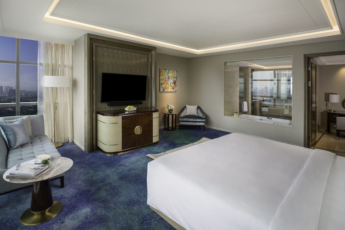 Habitación de hotel moderna con una cama grande, un sofá, un televisor, un escritorio y vistas a la ciudad.