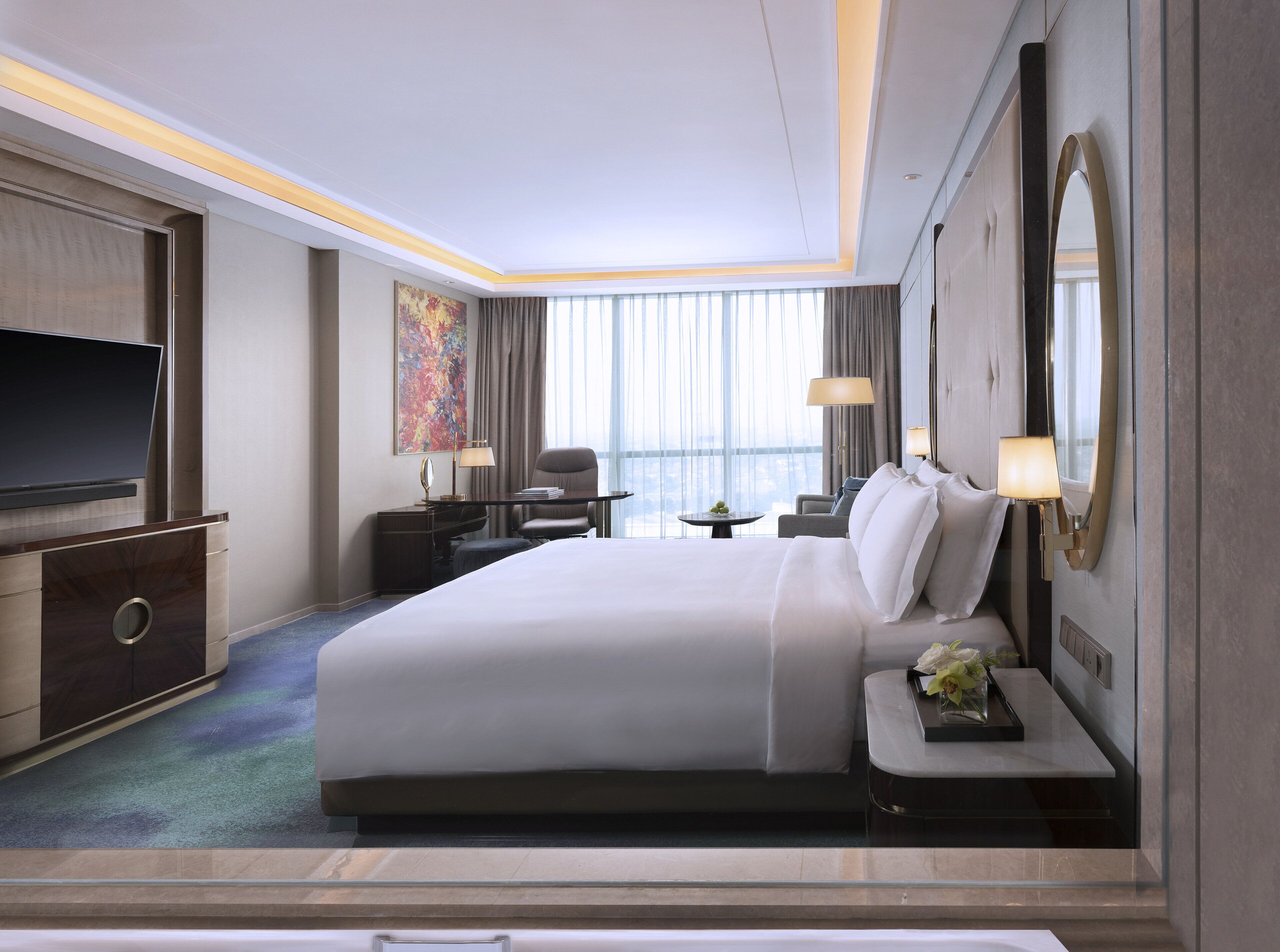 A hotel room with a large bed, a desk, a chair, a TV, and a window with curtains.