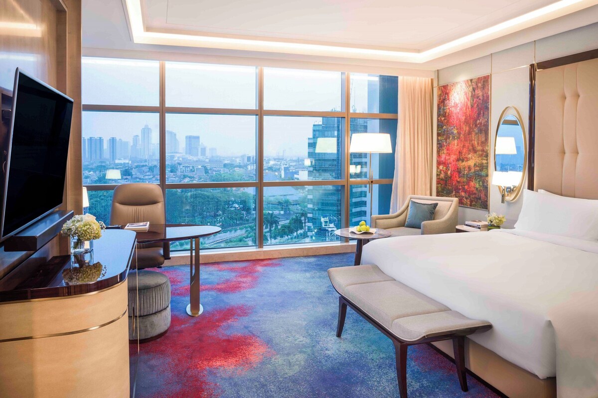 Habitación de hotel con un ventanal grande, una cama, un escritorio con televisor y una silla.