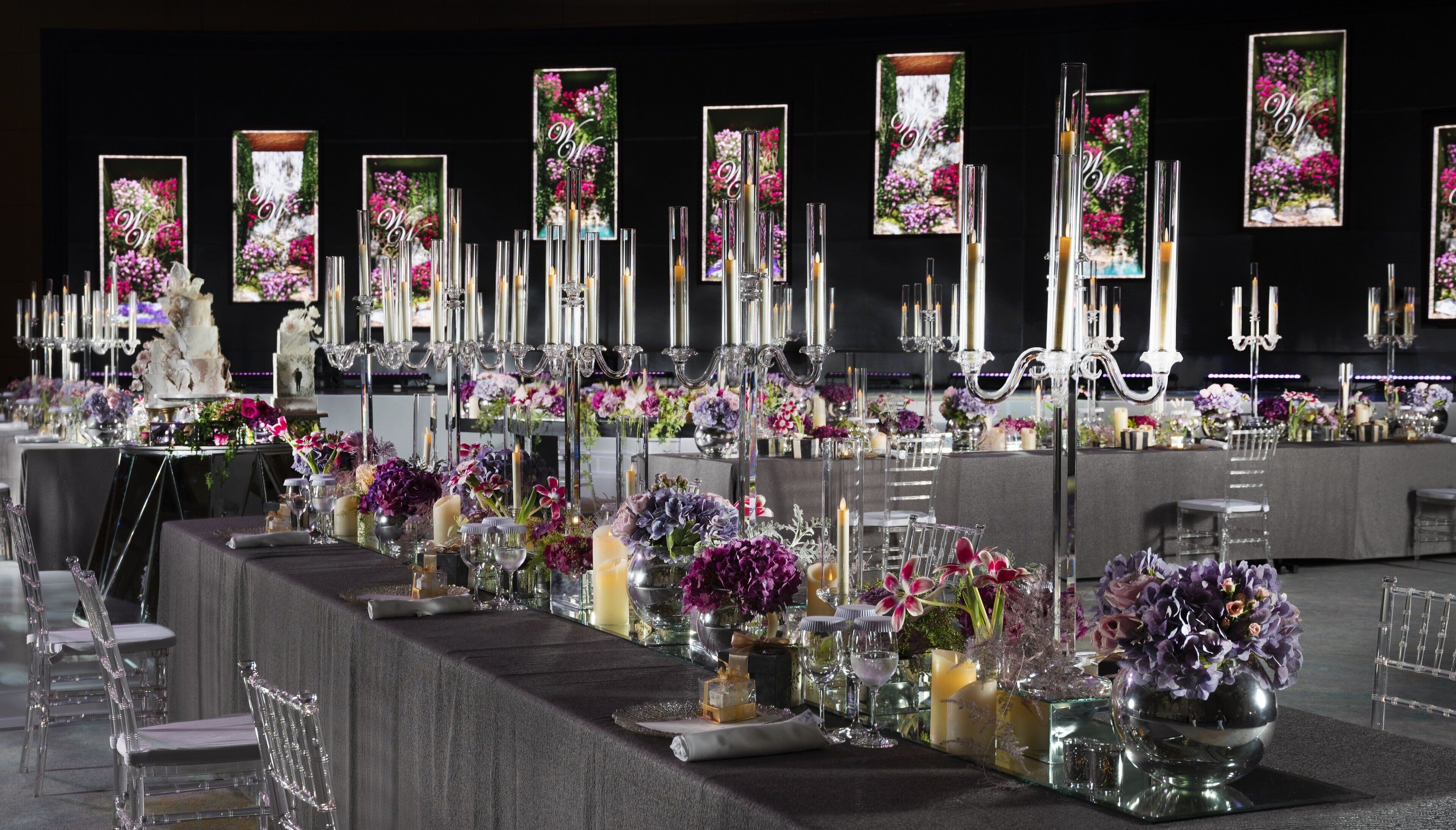 Ein festlich gedeckter Esstisch mit hohen Kerzenständern, klarem Glas und floralen Tischdekorationen.