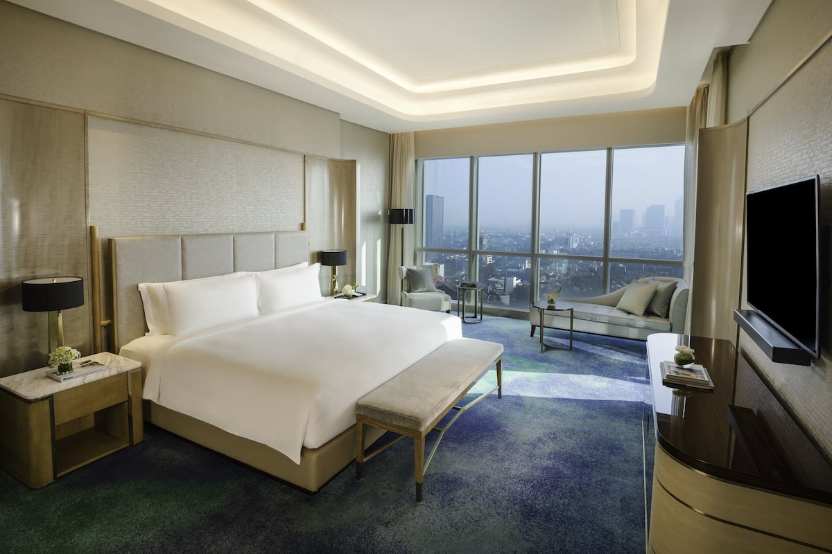Habitación de hotel moderna con una cama grande, un televisor de pantalla plana y vistas a la ciudad a través de amplios ventanales.