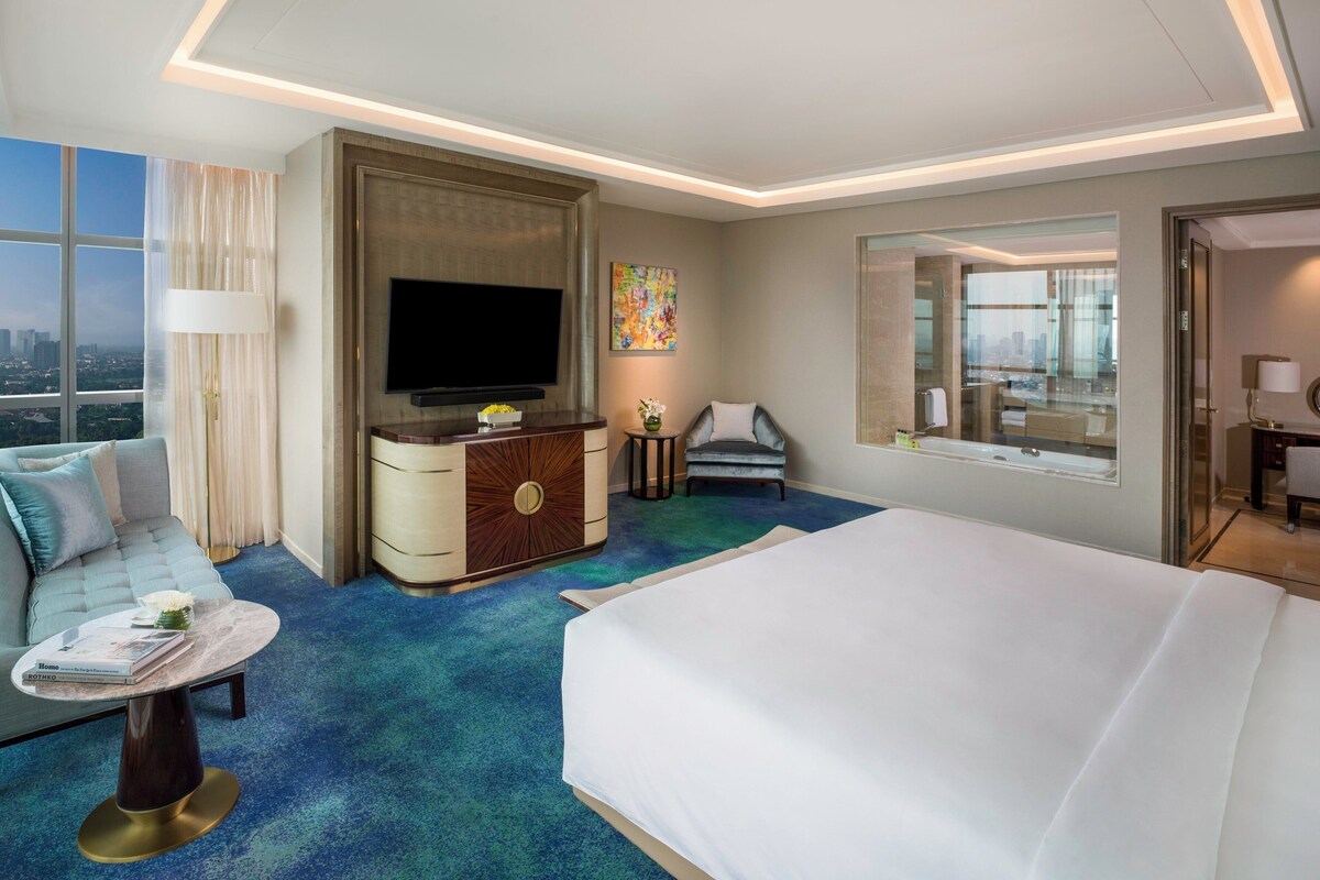 Habitación de hotel moderna con una cama grande, un sofá, un televisor, un escritorio y vistas a la ciudad.
