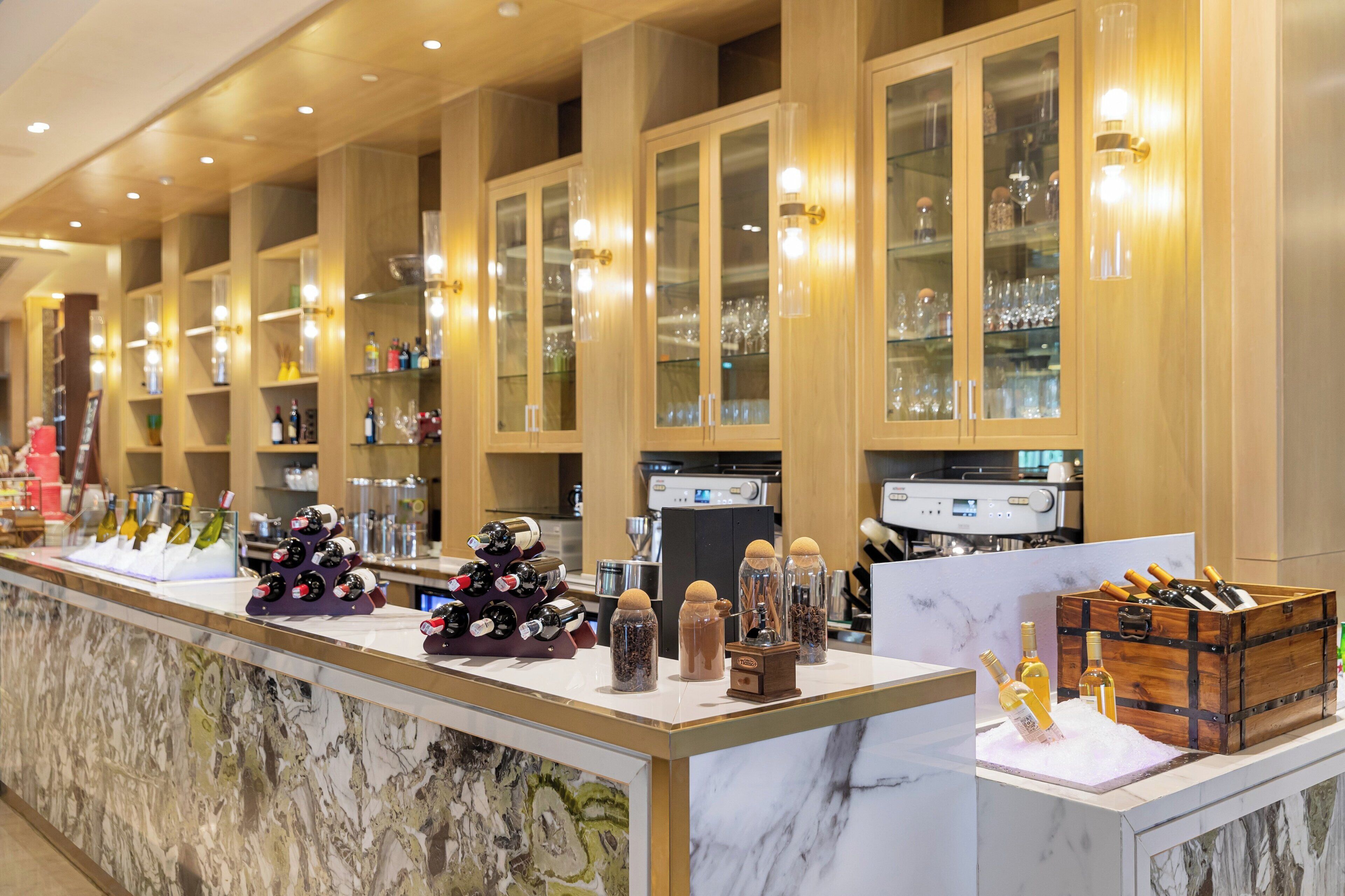 Un bar de hotel con encimera de mármol, botellas de vino y cristalería.