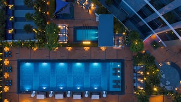 An aerial view of a hotel with a large rectangular pool, outdoor seating areas, and a modern building structure.