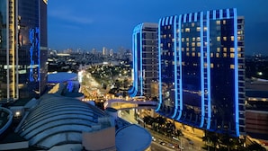 Un paisaje urbano al atardecer con edificios modernos y altos, uno de ellos con iluminación azul destacada.