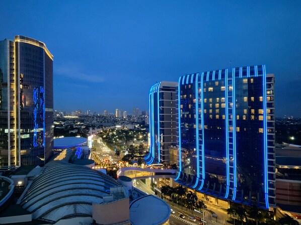 Un paisaje urbano al atardecer con edificios modernos y altos, uno de ellos con iluminación azul destacada.