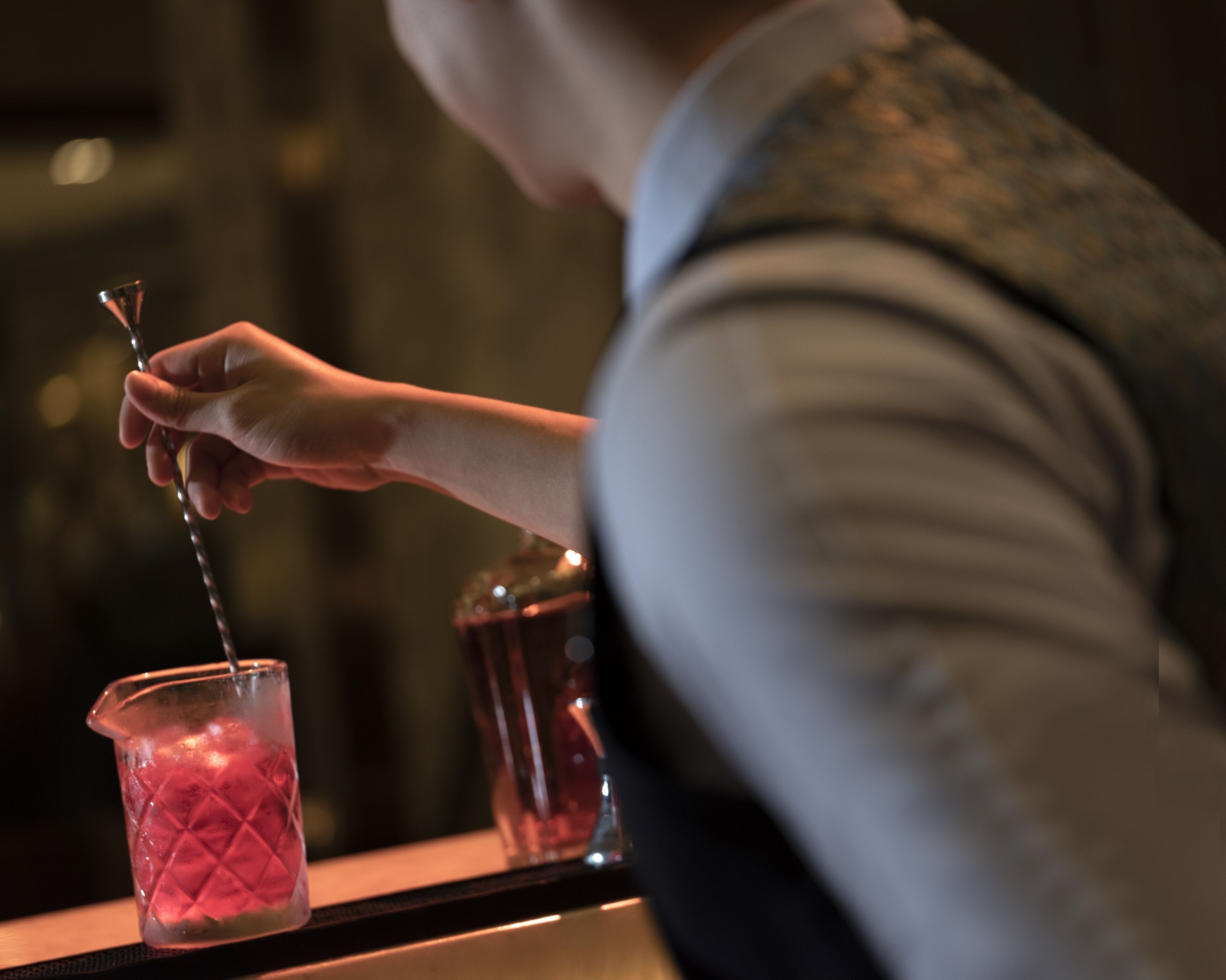 Una persona sirve una bebida desde un coctelera en un vaso.