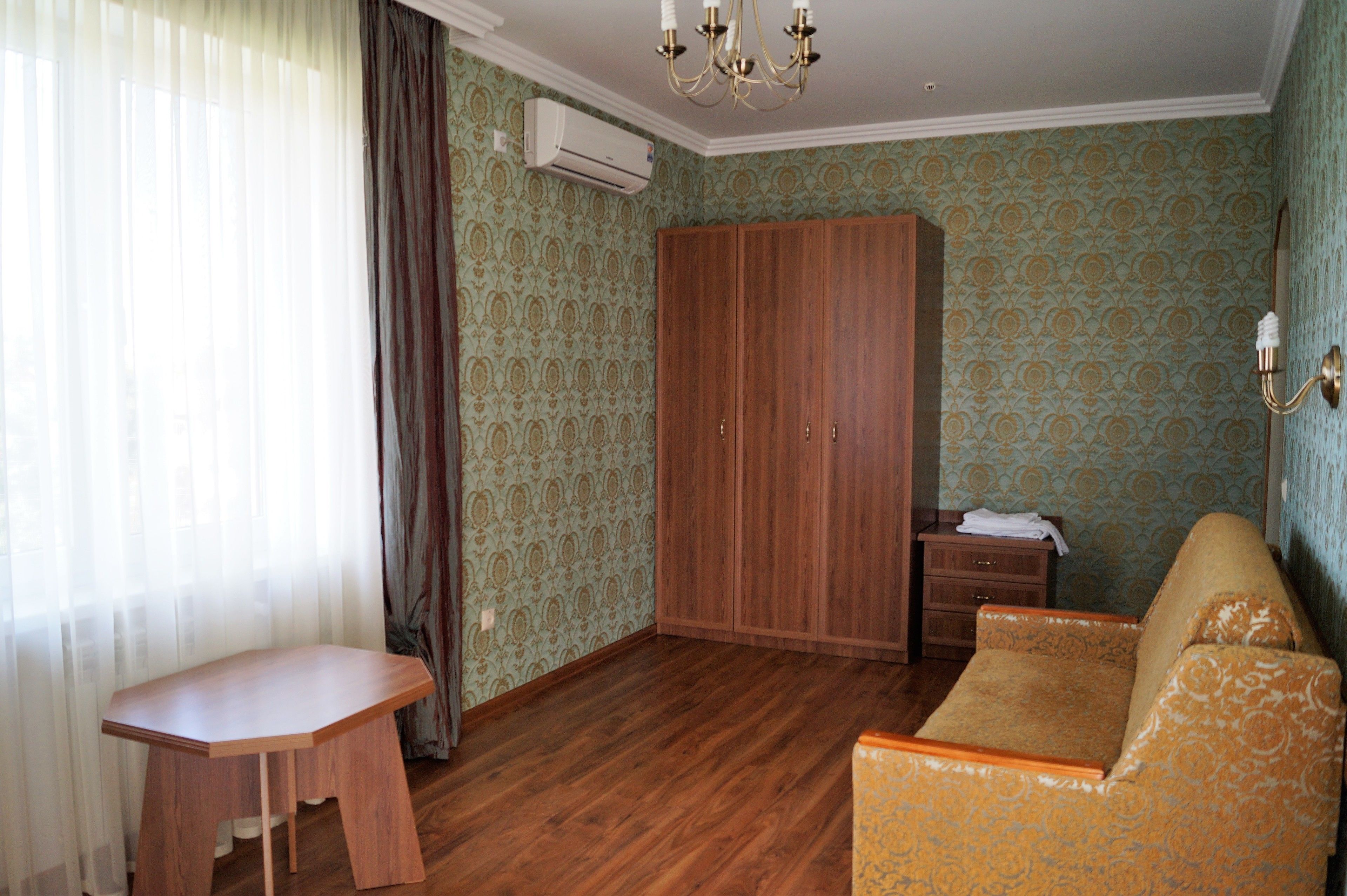 A room with a wooden wardrobe, a sofa, a small table, and patterned wallpaper.