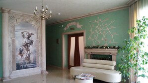 Un vestíbulo amplio con un mural clásico, una chimenea, un sofá y una planta en maceta.
