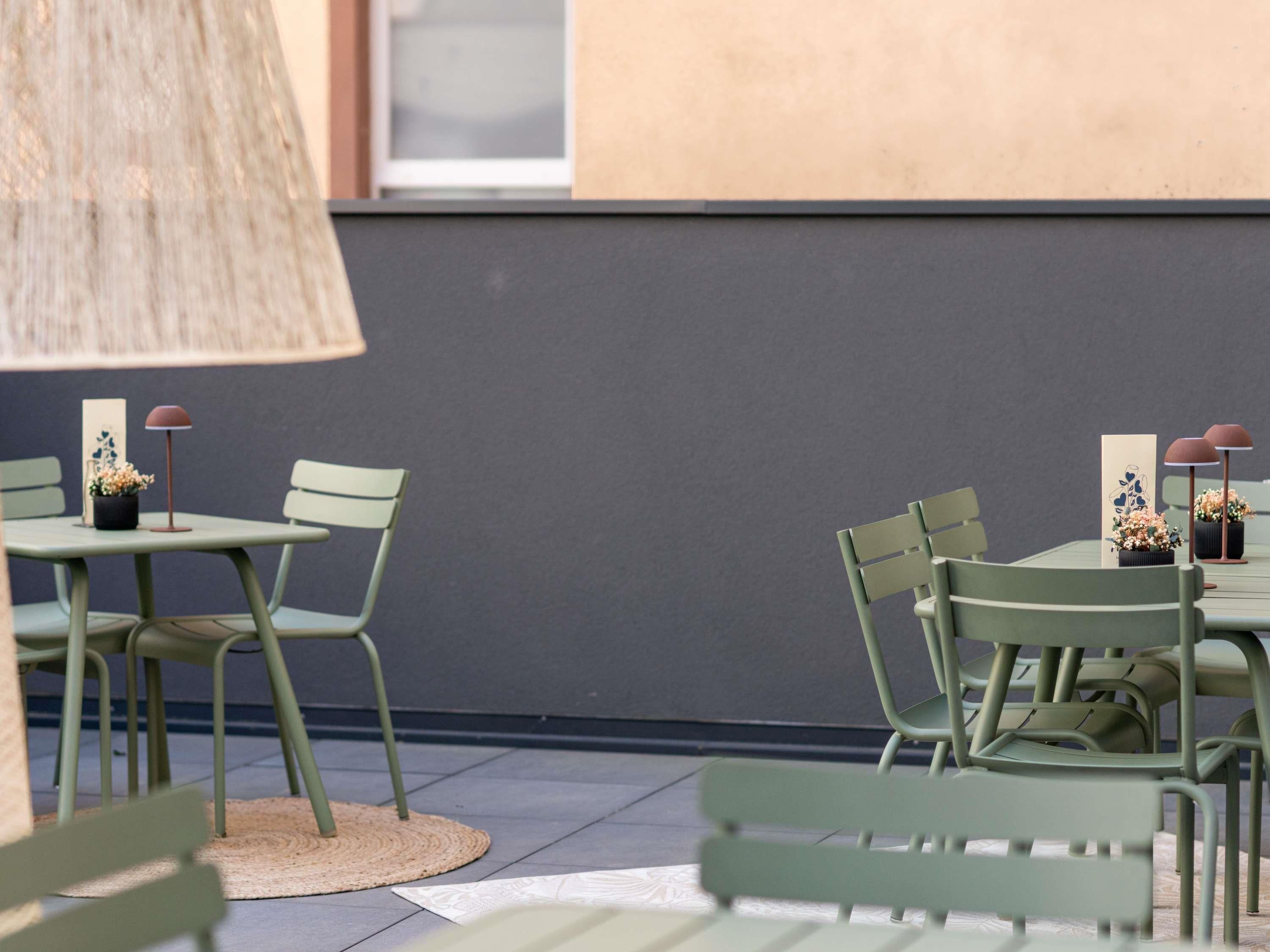An outdoor seating area with green chairs and tables, some with potted plants, and a woven lamp.