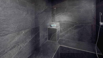 Une salle de bain moderne avec des carreaux de couleur foncée, une douche en verre et un pommeau de douche apparent.