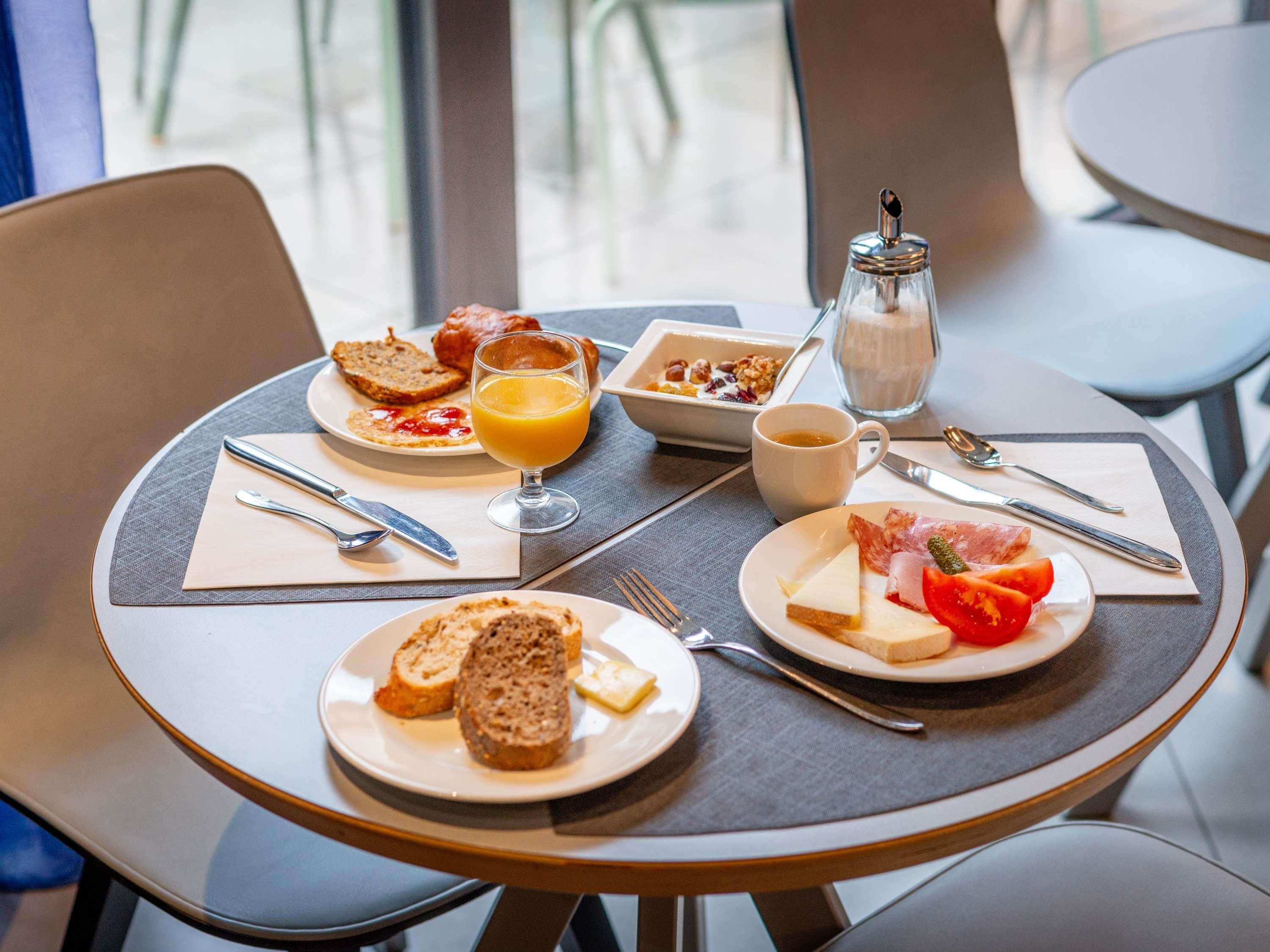 A breakfast table with plates of toast, fruit, cheese, and a glass of orange juice.